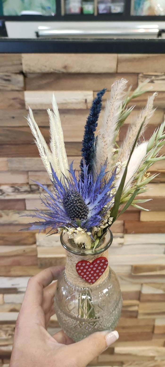 Petite composition de fleurs séchées bleu et blanc dans un flacon décoré d'un cœur